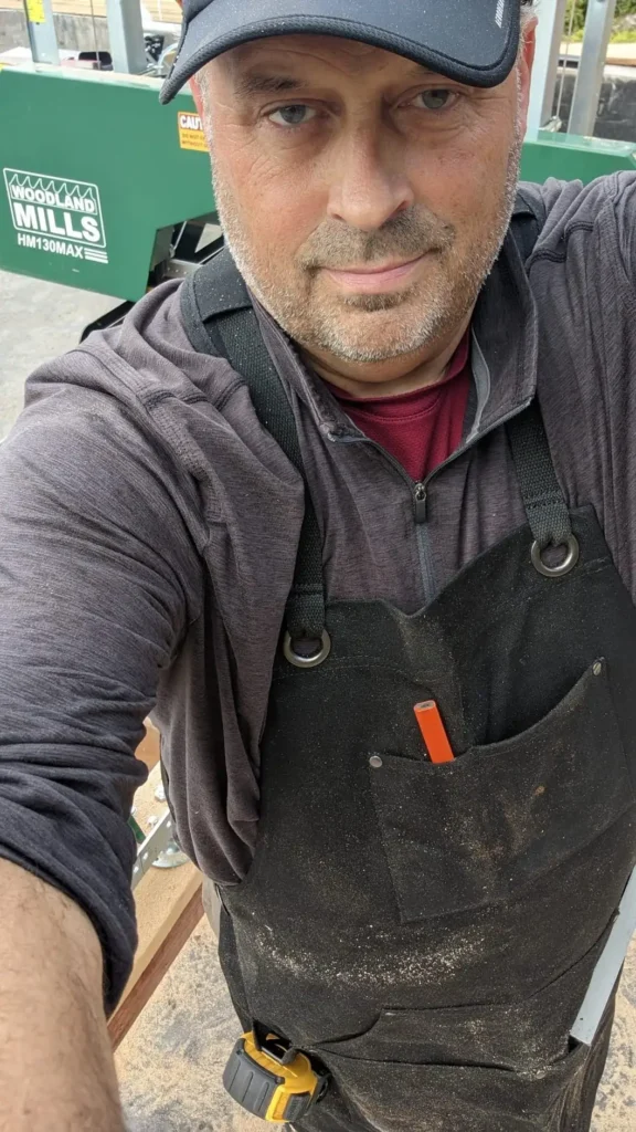 Woodworker selfie wearing a dark apron with pockets in a workshop.