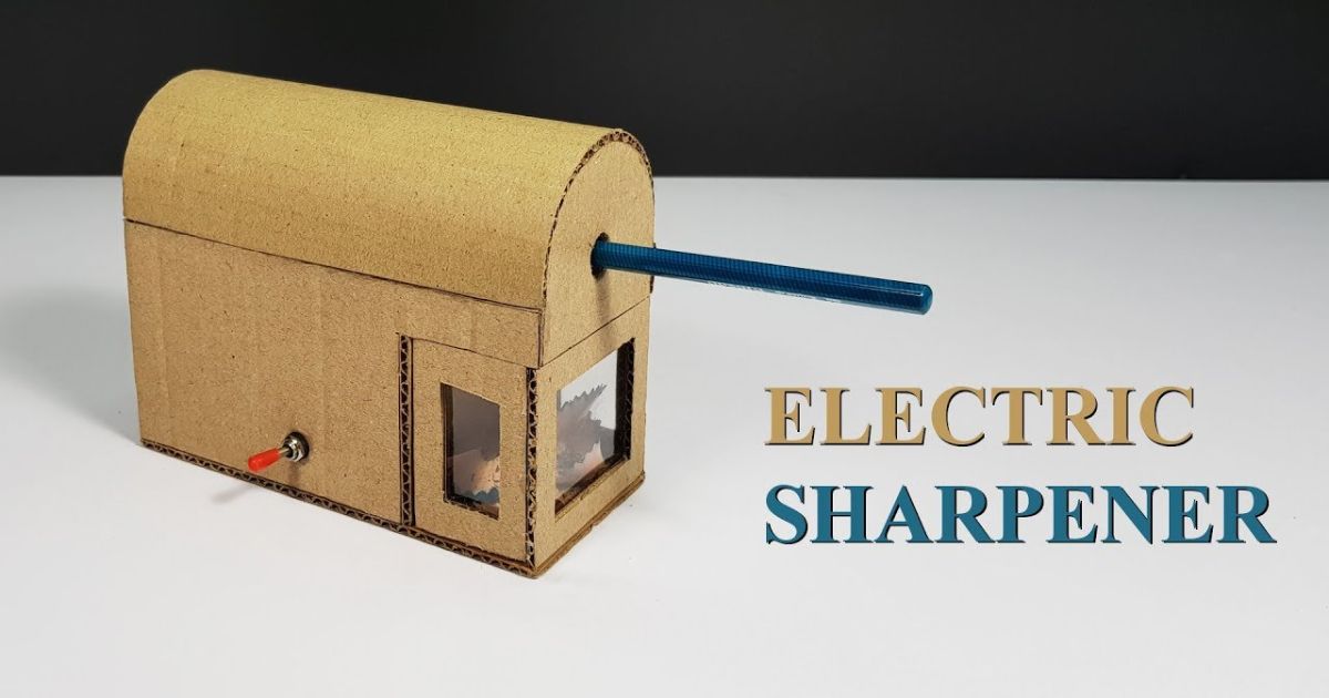 A homemade cardboard model of an electric pencil sharpener with a blue pencil inserted. It has a visible window for the sharpening mechanism and a red toggle switch on the side. The words "ELECTRIC SHARPENER" are on the right. How Does an Electric Pencil Sharpener Work_ in 5 Simple Steps