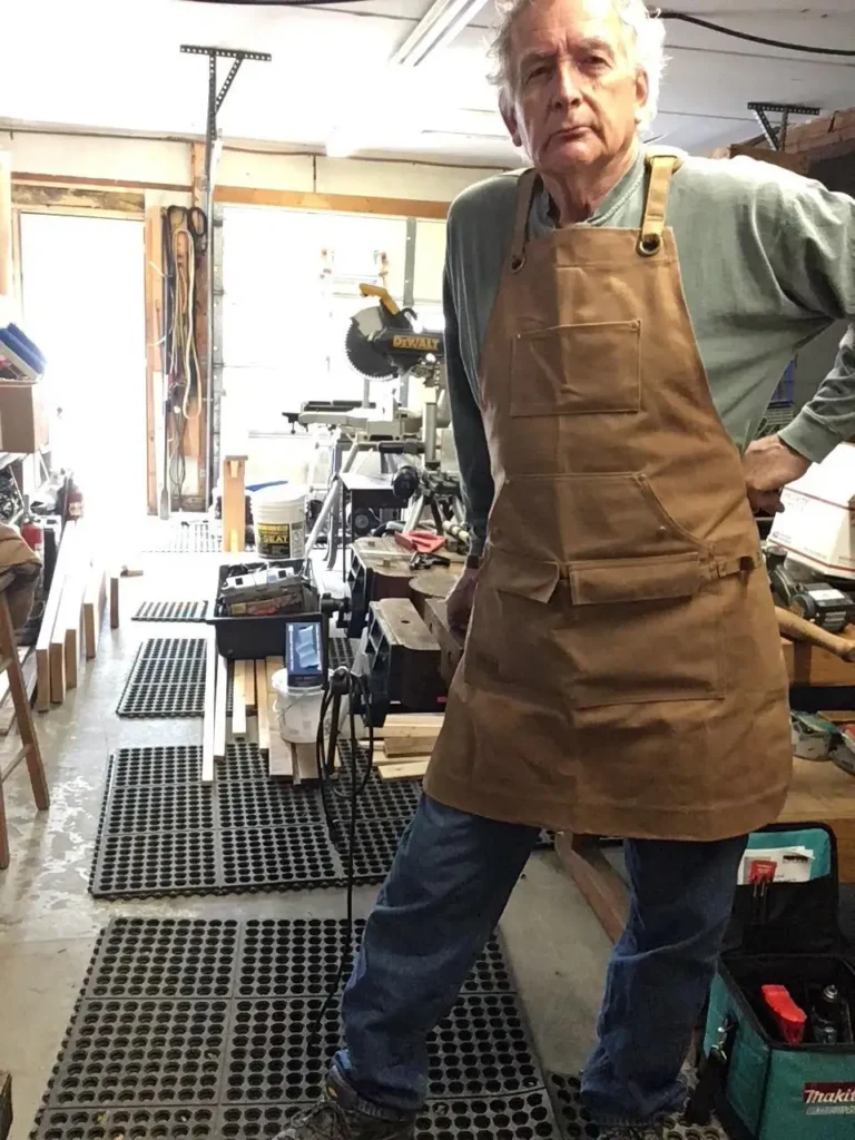 Woodworker wearing a brown apron in a workshop, expressing satisfaction.