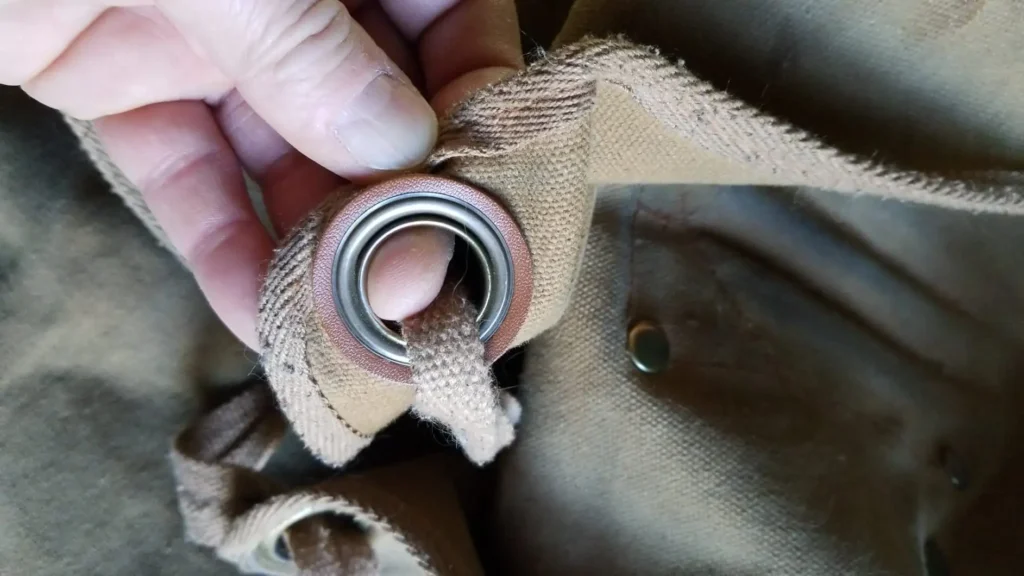 A hand holding the reinforced grommet and strap of a brown woodworking apron.